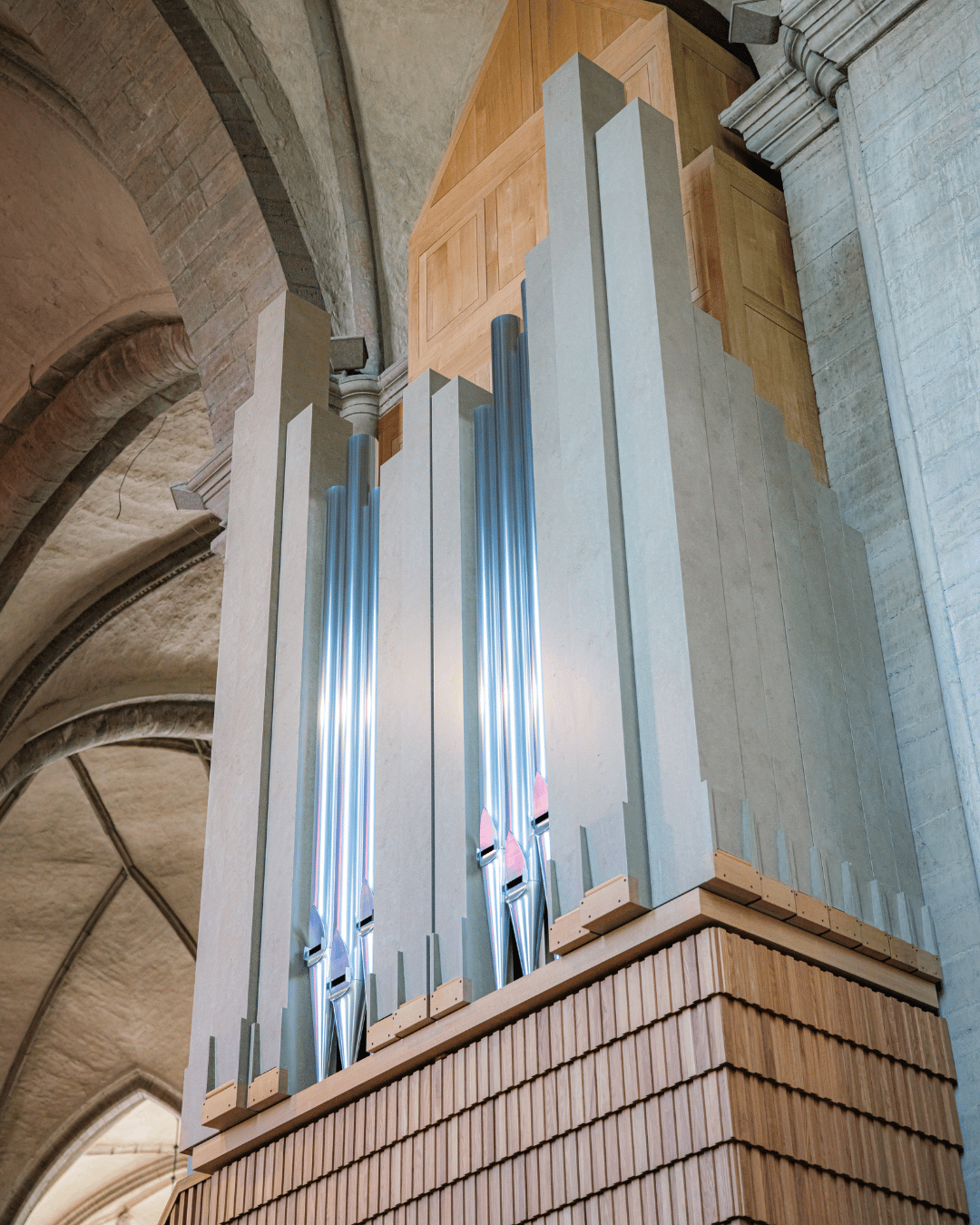 En stor piporgel med höga, glänsande silverpipor och en träbas står intill stenväggen i en kyrka med välvda tak.